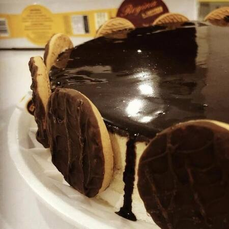 Torta c/ base de creme e baunilha coberta c/ ganache de chocolate ao leite e bolacha calipso ao redor.