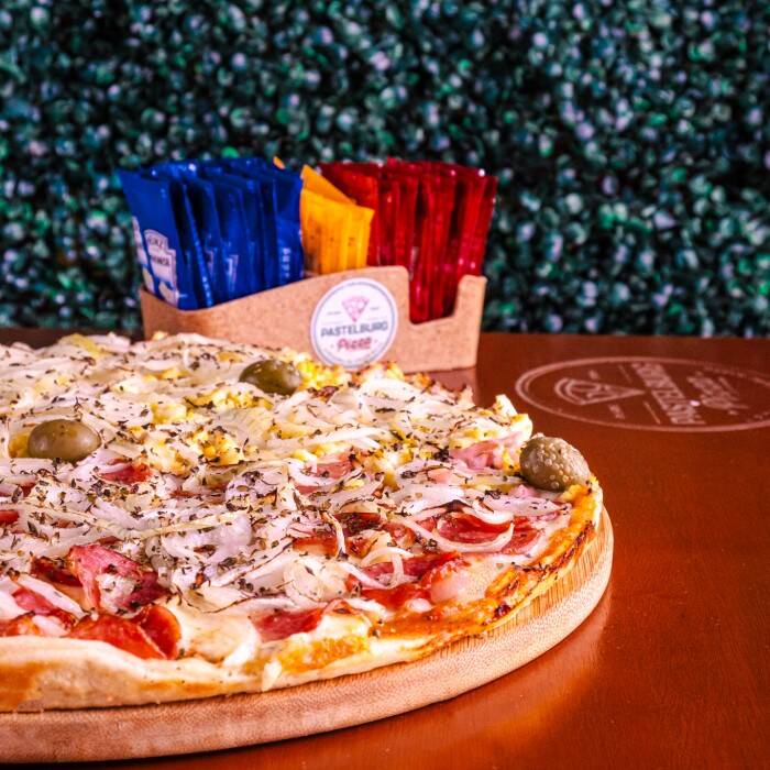 Saboreie nossa irresistível Pizza Grande, dividida harmoniosamente entre os sabores clássico da Calabresa, enriquecida com cebolas crocantes, e a tradicional Portuguesa, recheada com presunto de primeira, ovo, azeitonas saborosas e cebola. Tudo isso sobre um autêntico molho de tomate artesanal, coberto com uma generosa camada de mussarela derretida. Uma iguaria exclusiva para os paladares mais exi
