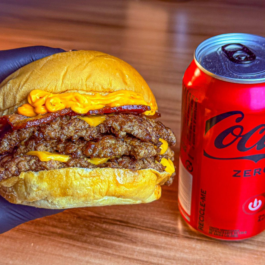 Pão brioche, 3 hambúrgueres smash de 70g, bacon, cheddar e maionese bodega. Acompanha coca cola lata caso queira trocar por coca cola zero favor colocar nas obs