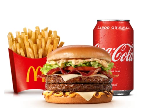 Dois hambúrgueres de carne 100% bovina, méquinese, a exclusiva maionese especial com sabor de carne defumada, alface e tomate, fatias de bacon, queijo processado sabor emental, molho especial e cebola ao molho shoyu, tudo isso no pão tipo brioche trazendo