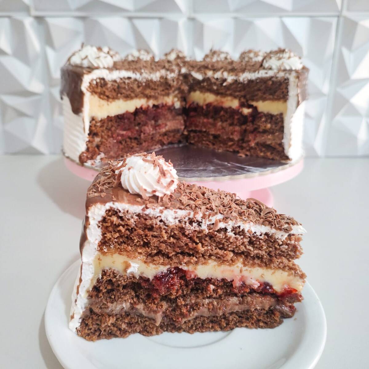 Fatia de Torta Floresta Negra: massa de chocolate fofinha, brigadeiro branco cremoso, geleia de cerejas suculentas e brigadeiro de chocolate em camadas. Uma fatia geladinha, intensa e irresistível para quem ama a combinação perfeita de chocolate com cereja.