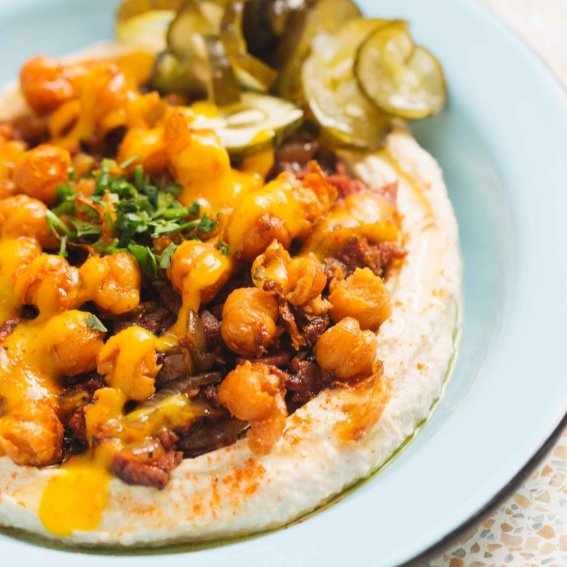 Hummus, pastrami, cebola caramelizada, grão-de-bico crocante, molho amba (a base de manga, curry e especiarias), picles de pepino, azeite e páprica.