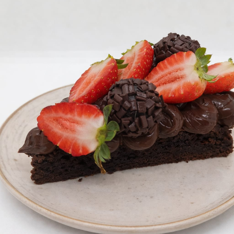 Fatia generosa de brownie de chocolate, super macio e intenso, finalizada com cobertura cremosa de brigadeiro, morangos frescos e brigadeiros de chocolate. Um clássico repaginado, elegante e irresistível- do jeito que um bom brownie merece!!