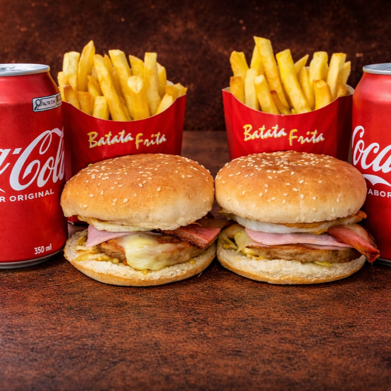 2 X-Tudo com pão de gergelim, carne, bacon, ovo, queijo mussarela, presunto, cheddar e batata palha + 2 Batata-frita + 2 Coca Cola Lata