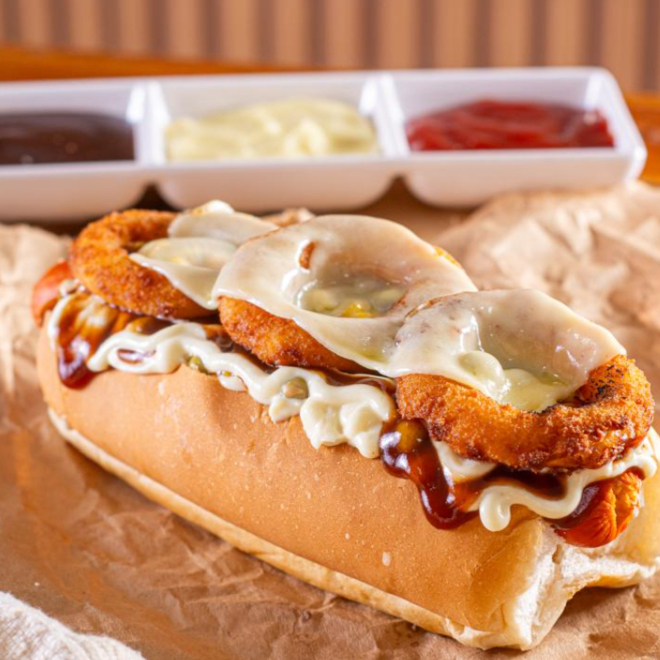 Pão, salsicha, maionese especial, barbecue, milho, ervilha, tomate, cebola empanada, e mussarela maçaricado.