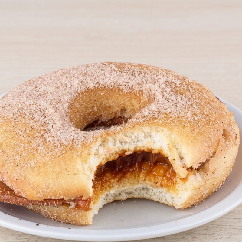 Donuts macio com açúcar e canela que remetem ao churros clássico, recheado com doce de leite cremoso. Sabor nostálgico e aconchegante. Peça agora!