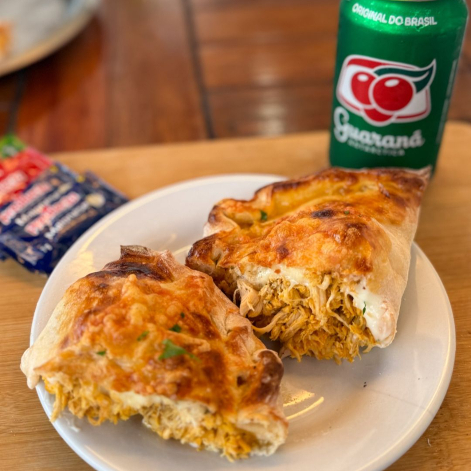 Calzone de frango com requeijão e muçarela, feito com massa leve e dourada, assado na medida certa. Recheio cremoso, suculento e bem servido, com frango desfiado temperado e muito queijo derretido. Perfeito pra quem quer um lanche saboroso e que satisfaz de verdade!