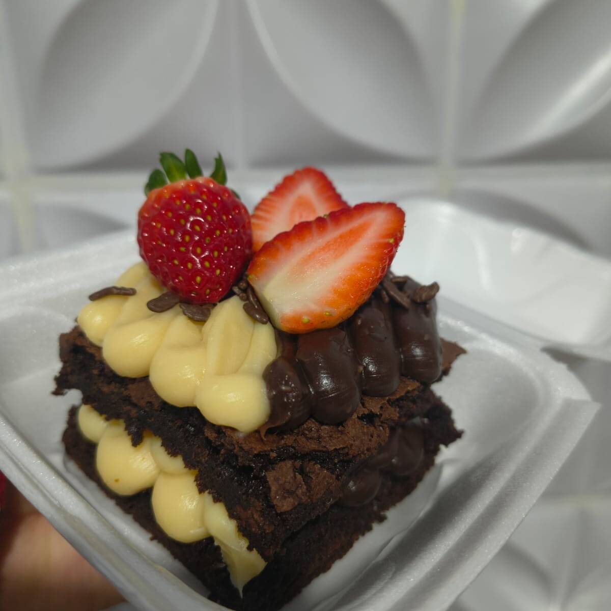 Brownie clássico Double, recheado com brigadeiro de ninho e brigadeiro de chocolate, finalizado com morangos.