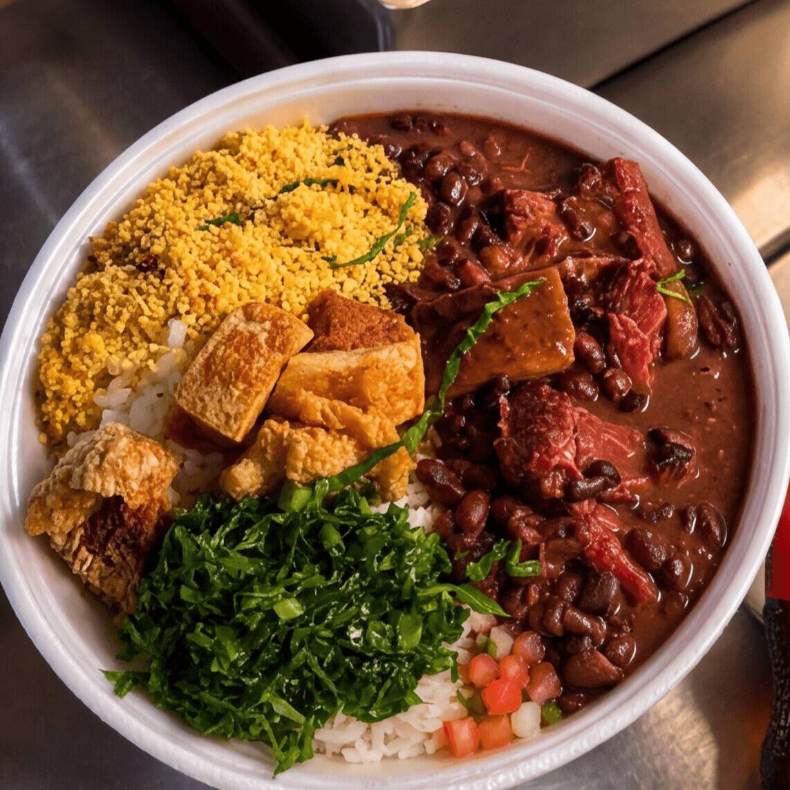 Arroz, feijoada caprichada (calabresa, bacon e costelinha), farofa de cebola, couve refogada no alho e laranja.
