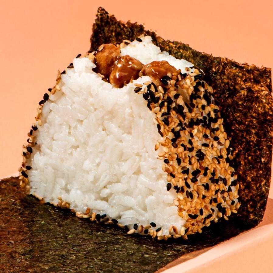 Bolinho de arroz Shari, recheado com frango ao molho teriyaki e um toque de óleo de gergelim, envolto por um mix de gergelim e acompanhado de alga nori, embalada separadamente para manter a crocância até o momento de consumo.