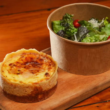 Tradicional massa de quiche com recheio de bacon, gruyere e creme de leite. Acompanha salada de mix de folhas verdes, parmesão ralado e tomate cereja.