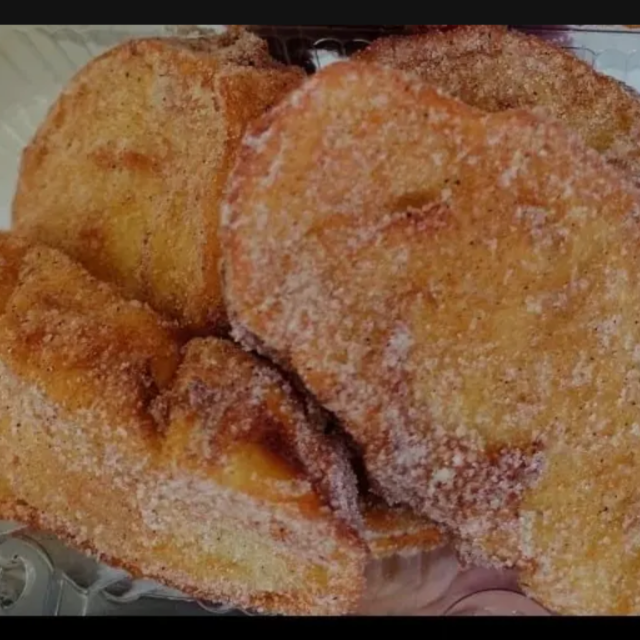Fatia de pão empanada e frita (rabanada), com crosta bem dourada, polvilhada com abundante açúcar e canela.