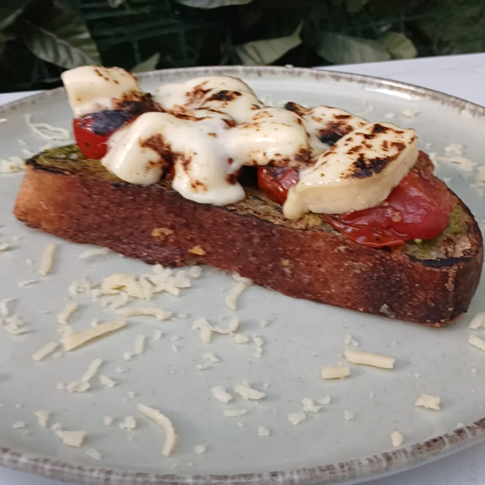 Fatia de Sourdough tostada na manteiga, pesto de manjericão, tomates confitados, e queijo minas gratinado;