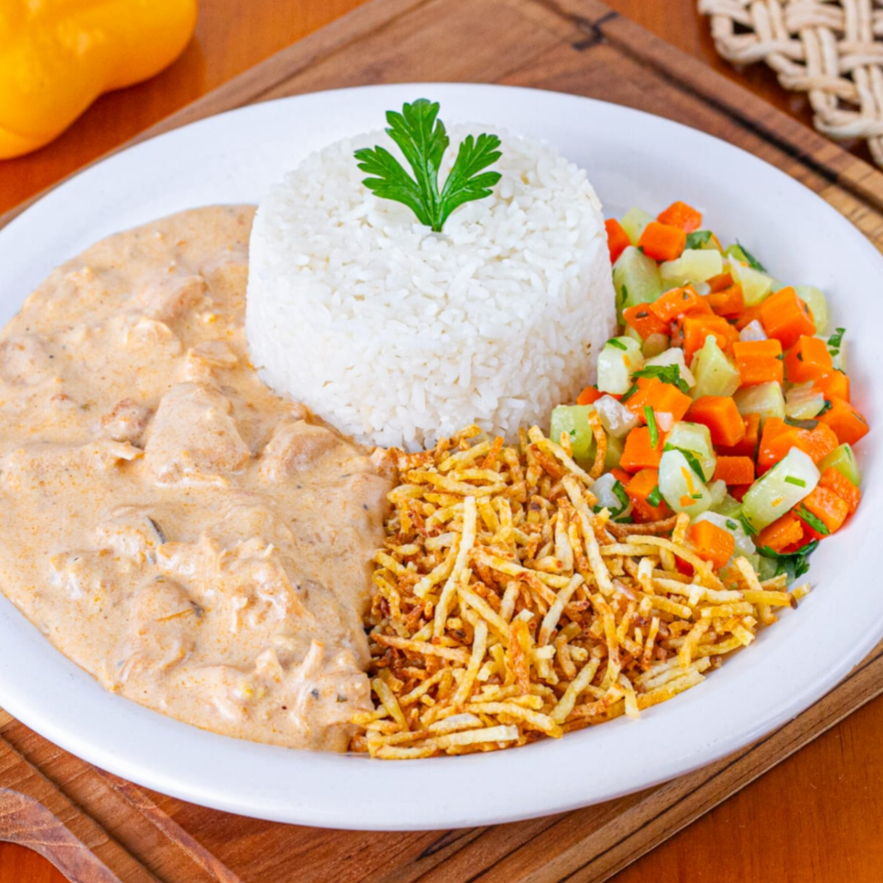 Sugestão do Chef em Pratos Premium: 'Marmitex de Strogonoff de Frango com Batata Palha e Salada de Legumes'. Uma refeição deliciosa e satisfatória de strogonoff, preparada com filé de frango suculento, cortado em cubos e misturado a um molho cremoso. É acompanhado de um arroz branco perfeitamente soltinho e uma batata palha crocante. Para completar, uma salada de legumes, composta por cenoura e chuchu, temperada na medida certa. Tudo isso é generosamente servido em uma marmitex com aproximadamente 600gr, servindo muito bem a 1 pessoa, garantindo uma refeição completa e saborosa