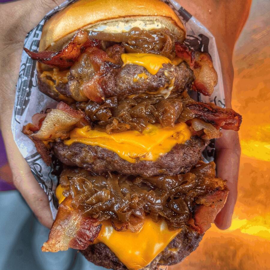 O Júpiter é o lanche definitivo para quem busca uma experiência monumental e sem limites, servido em nosso pão brioche premium, extremamente amanteigado e selado com perfeição. Este gigante é um verdadeiro festival de sabor, composto por três hambúrgueres artesanais de 150g cada, totalizando 450g de carne suculenta. A estrutura é montada com três camadas de queijo cheddar derretido, três camadas de bacon crocante e três camadas de nossa cebola caramelizada artesanal, garantindo intensidade em cada mordida. Tudo isso é envolvido pela nossa exclusiva maionese verde da casa, criando uma combinação poderosa e irresistível para os verdadeiros corajosos.