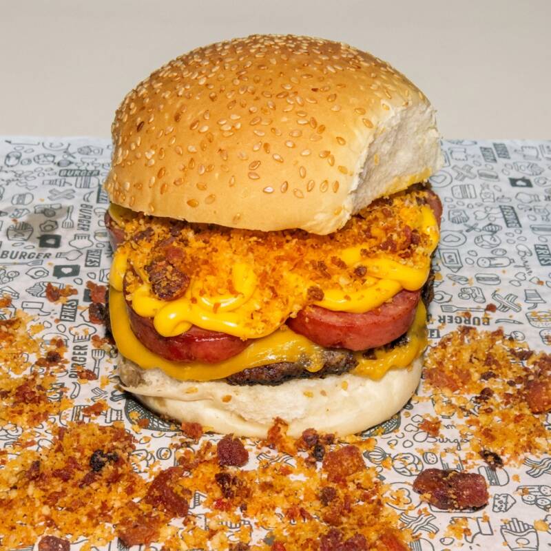Pão manteigado, carne de 145g, queijo cheddar, calabresa, cheddar e farofa de bacon com farinha panko.