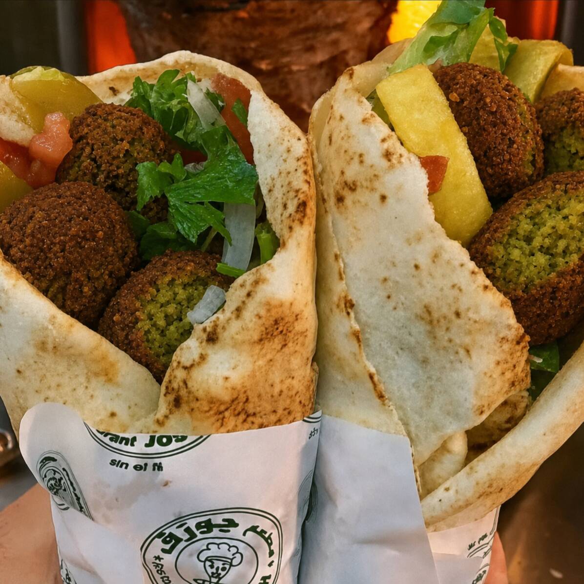 Dois shawarmas de falafel no pão sírio, preparados com creme de alho, alface, tomate, cebola e batata frita dentro do lanche.
