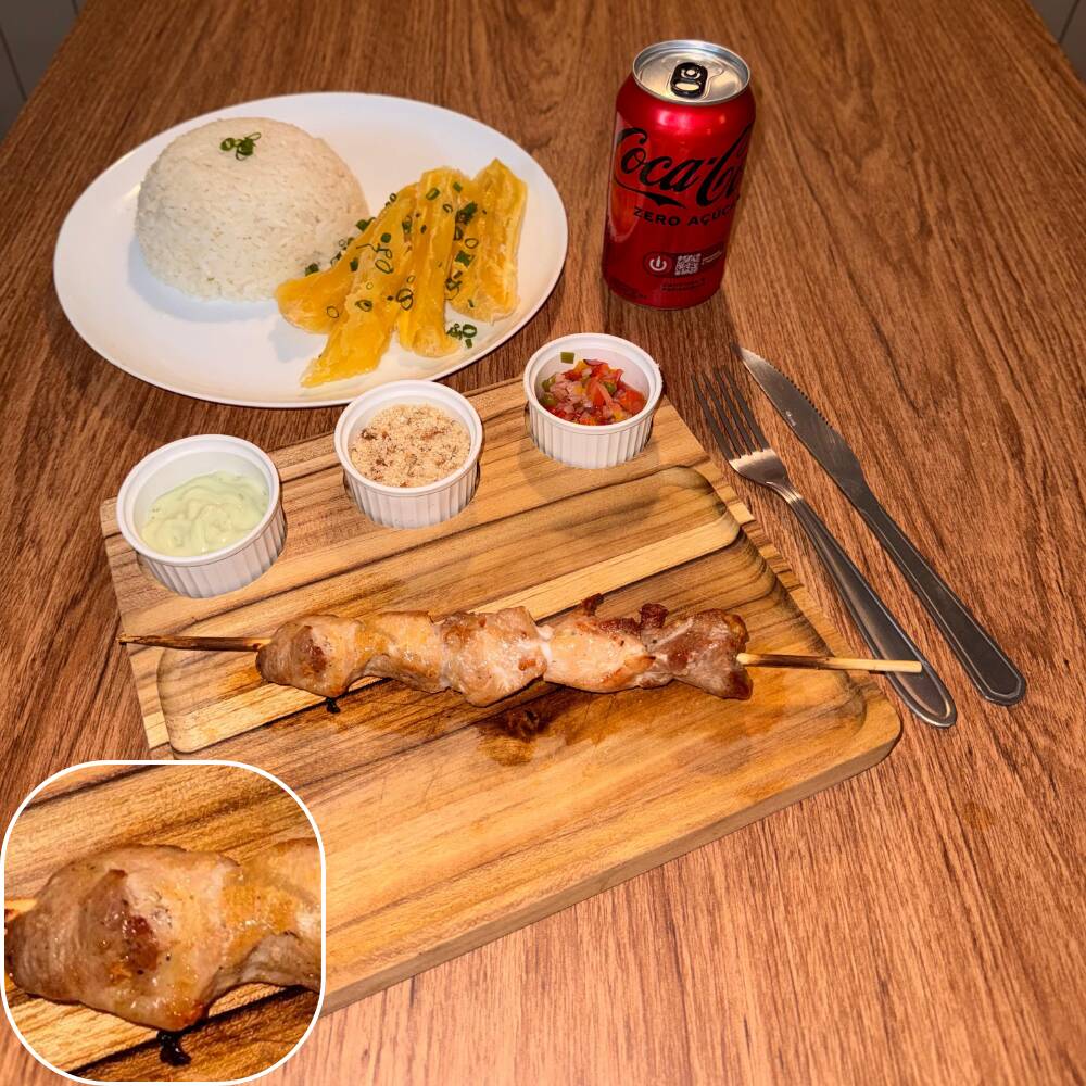 Espeto de lombo suíno acompanhado por arroz, mandioca, vinagrete, farofa crocante e molho verde.