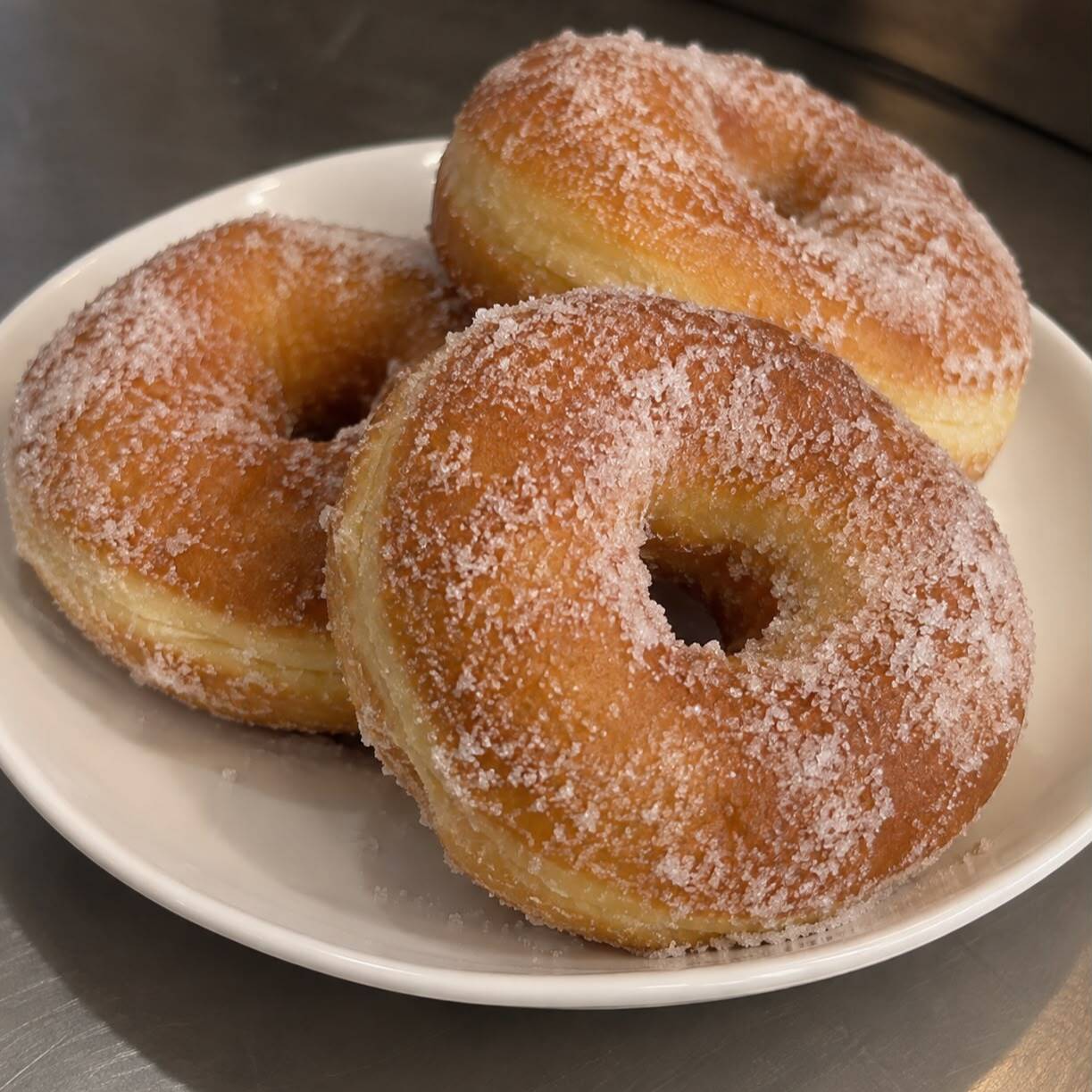 Rosquinha macia, levemente dourada e envolvida em açúcar, perfeita para acompanhar um café.