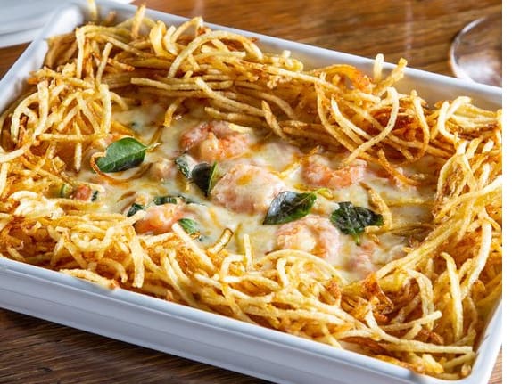 Camarões refogados com alho e cebola, servido sobre cremoso arroz com manjericão, envolvido com molho branco. Gratinado com queijo muçarela. Acompanha batata palha. tamanho do camarão nesse prato: 13g