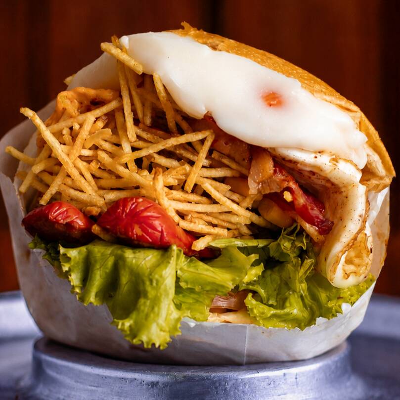Pão macio com filé de frango grelhado, muçarela, presunto, bacon crocante, salsicha, Catupiry cremoso, alface, tomate, milho verde e batata palha. Completo e irresistível.