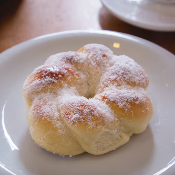 Rosca doce, feita com massa leve e macia, coberta com uma camada generosa de coco ralado e leve toque de açúcar. Um clássico da padaria, com sabor suave e textura que desmancha na boca.