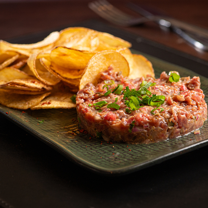 Filé bovino picado na ponta da faca, temperado com mostarda dijon, alcaparras, picles e gema fresca, servido com chips de batata crocante.