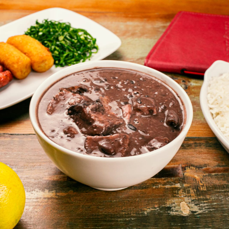 Feijoada com arroz branco, farofa com bacon, couve refogada, banana a milanesa, mini linguiças e laranja.