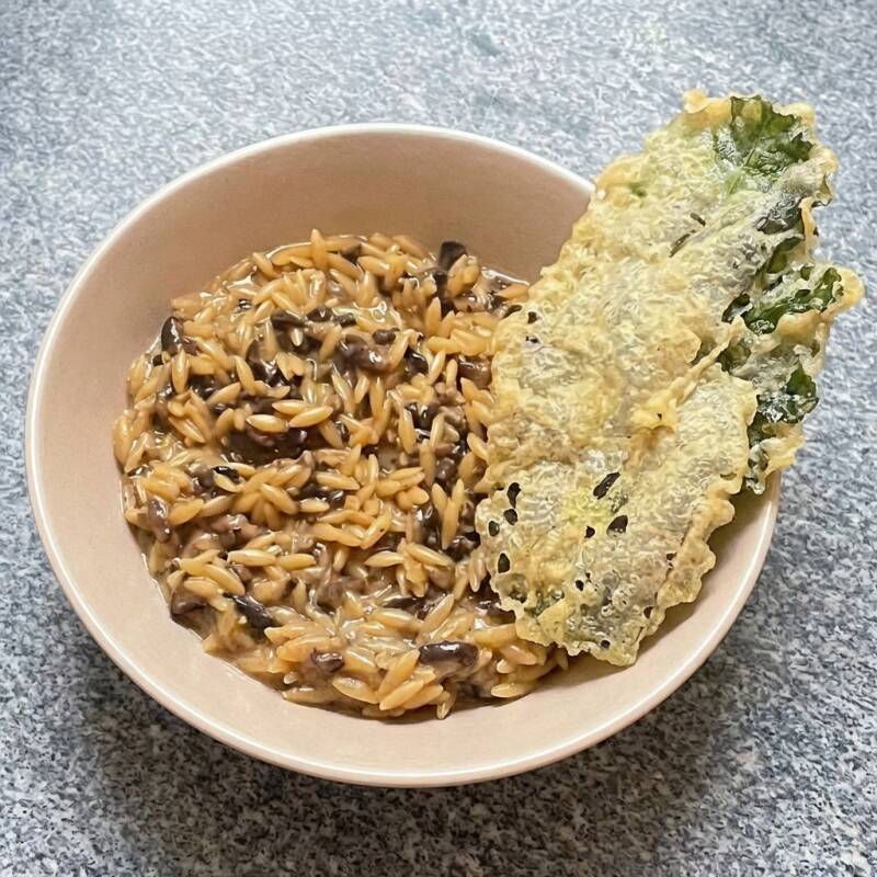 Massa em formato de arroz com cogumelos frescos (shitake, cogumelo Paris e cogumelo Portobelo), creme de leite fresco, queijo parmesão e fundo de legumes. Acompanha um tempura de couve. (A tempurá de couve é um adereço do prato servido em nosso restaurante que pode sofrer avarias no transporte mas achamos que o cliente gostaria de recebê-la também ;) vegetariano, Veg, fit, saudável, cremoso, confort.