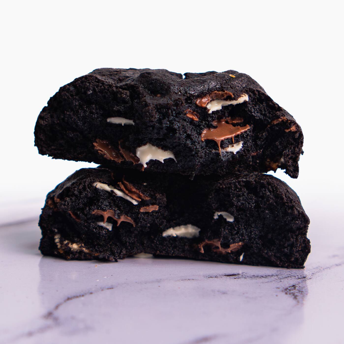 Nosso cookie de Triplo Chocolate tem massa de cacau black e é recheado com uma mistura irresistível de chocolate nobre ao leite e branco, trazendo intensidade, equilíbrio e criando um contraste único de sabores.