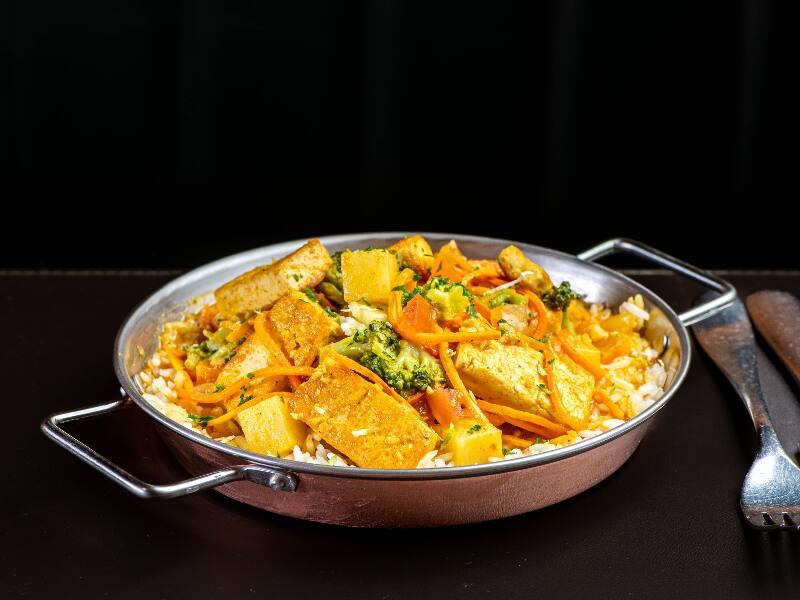 Tofu marinado com curry e páprica defumada, refogado com azeite de oliva, alho, cebola, gengibre e pimenta do reino, com molho de curry ao leite de coco com batata, cenoura, brócolis, tomate e toque de limão. Servido sobre uma cama de arroz branco e