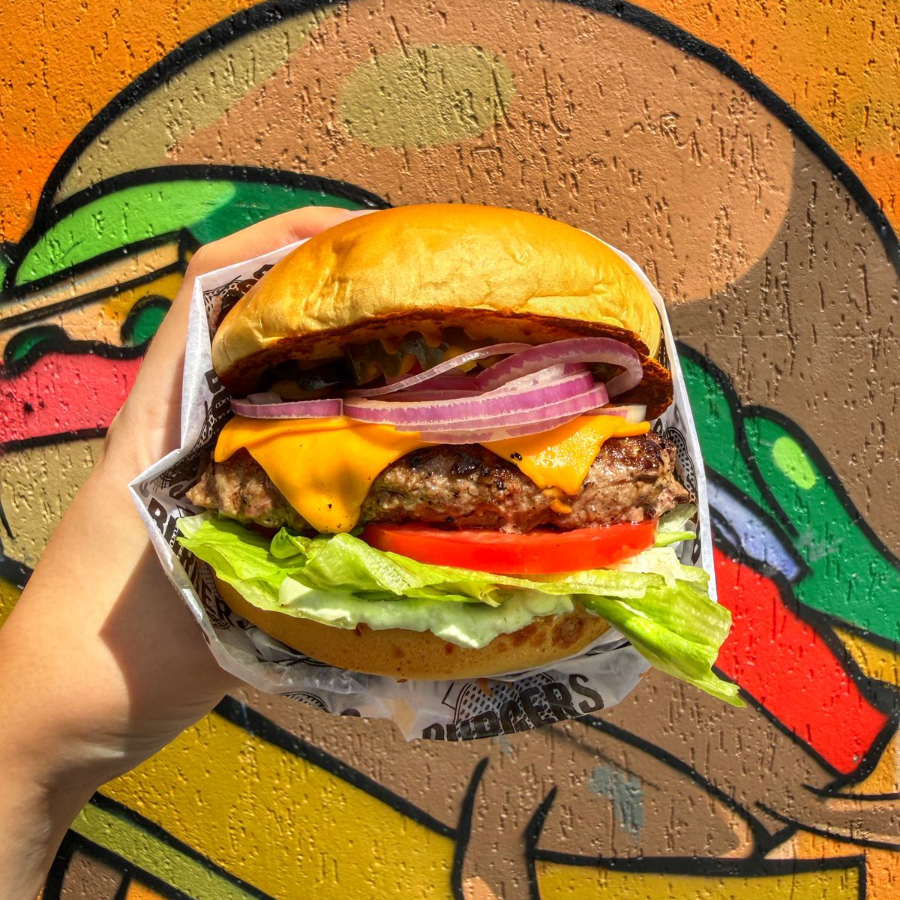 Pão brioche tostado na chapa com manteiga, hamburguer artesanal de aprox 160g, queijo cheddar fatiado, alface, tomate, picles, cebola roxa e maionese da casa.