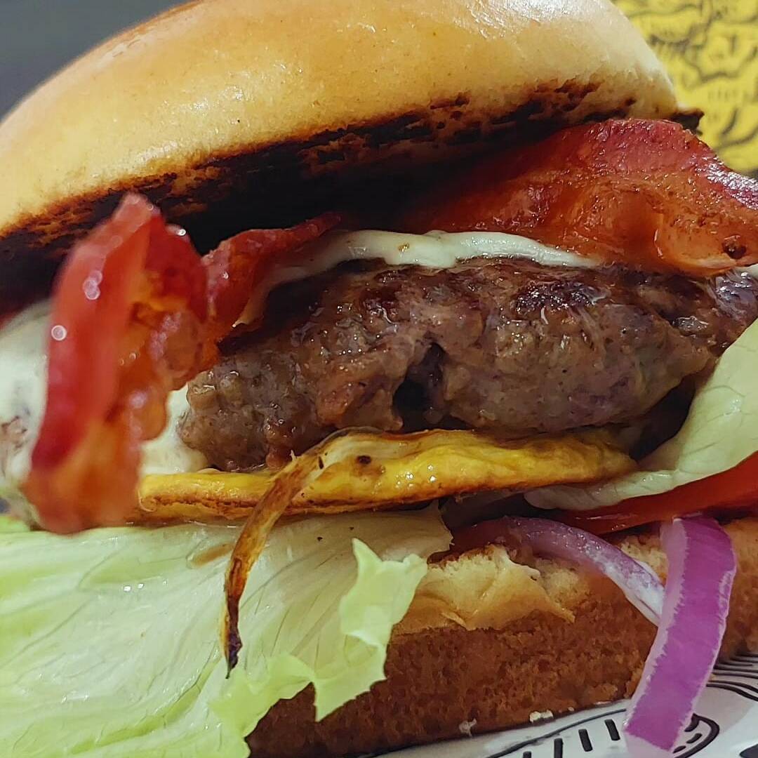 HAMBÚRGUER ARTESANAL DE 180 g, ACOMPANHADO COM QUEIJO MUSSARELA DERRETIDA, TIRAS DE BACON CROCANTE, OVO, SERVIDOS COM SALADA DE ALFACE, TOMATE E CEBOLA ROXA EM NOSSO DELICIOSO PÃO BRIOCHE PRODUZIDO NA CASA, E MAIONESE CASEIRA