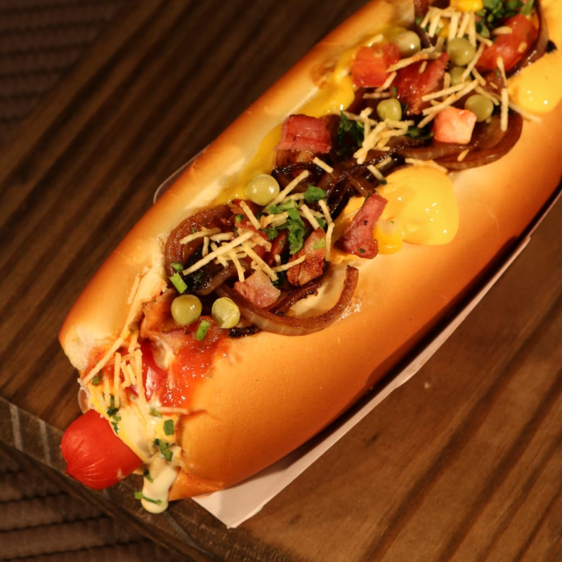 Pão, salsicha, molho de tomate, molho cheddar, bacon, cebola, maionese, ketchup, mostarda, molho mil ilhas, tomate, milho, ervilha, salsa, queijo parmesao e batata palha