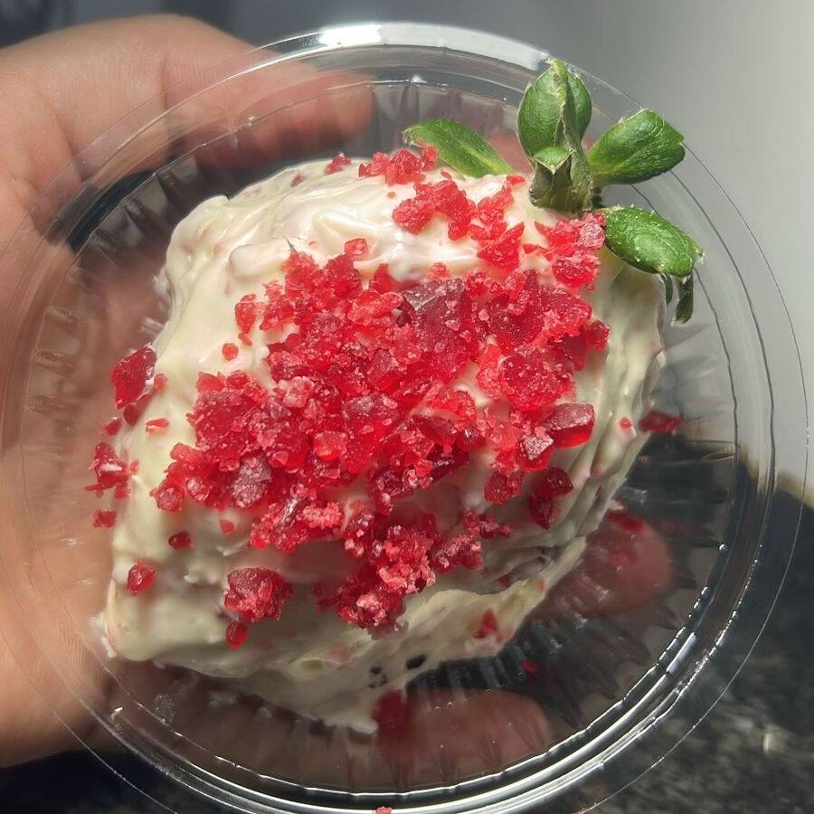 Morango fresco com recheio de ninho coberto por chocolate branco com açucar cristalizado cravejados em volta.