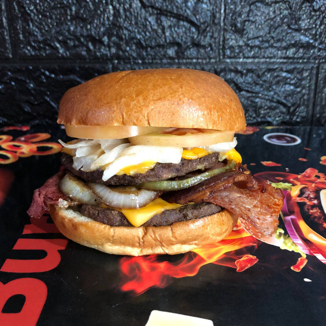 Pão brioche selado na chapa, duas carne bovina de 100g preparada na grelha, bacon, queijo cheddar fatiado, picles, alface americana, tomate, cebola caramelizada e molho opcional.
