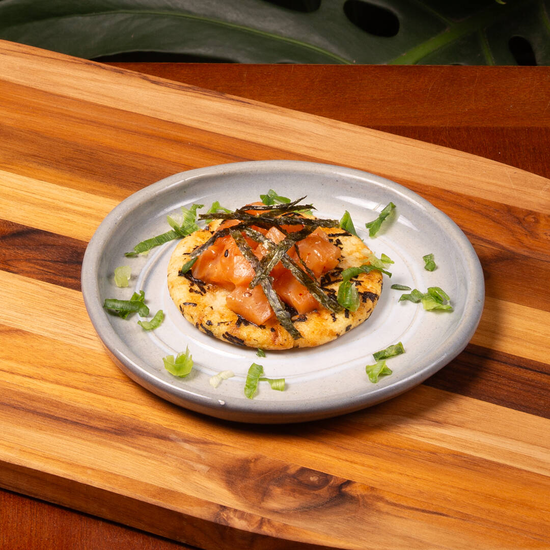 Um sucesso de nossos restaurantes! Tartare de salmão fresco com um leve toque de maionese de sriracha sobre um crocante biscoito senbei (feito de algas e arroz). Porção de 30g de salmão.