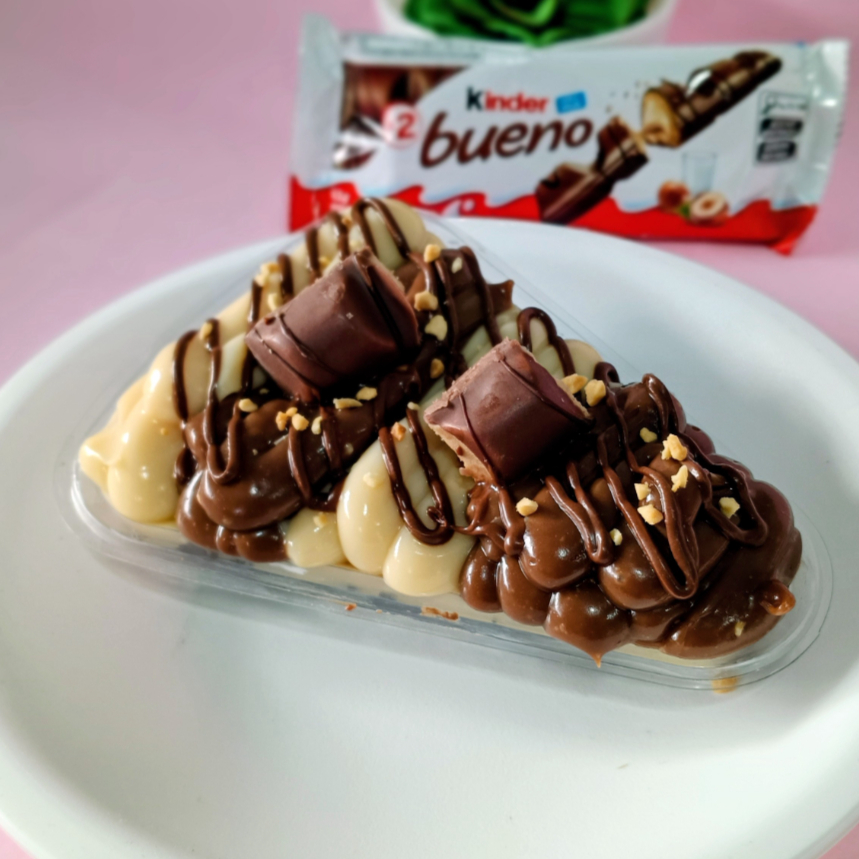 Uma fatia de pizza de brownie úmido com recheios intercalados com recheio branco e um recheio avelã confio de Nutella e claro o bombom kinder Bueno que não pode faltar!!