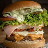 Para quem quer um lanche completo e cheio de sabor! Nosso pão brioche macio envolve uma carne suculenta, coberta por muito queijo derretido, bacon crocante e presunto bem servido. O ovo traz cremosidade, enquanto alface e tomate equilibram o lanche. Acompanha batata frita crocante. Ingredientes: • Pão brioche artesanal; • Carne de hambúrguer grelhada; • Queijo derretido na medida certa; • Bac