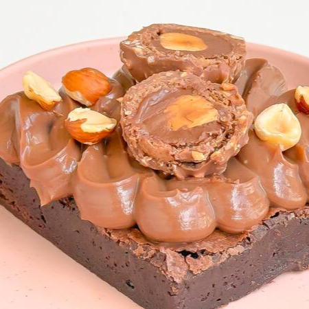 Brownie chocolatudo coberto com brigadeiro cremoso, bombom Ferrero Rocher e pedaços de avelã. tamanho 7x7cm