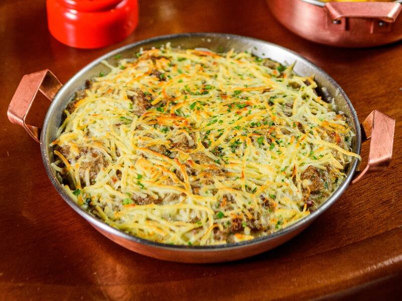 Arroz de leite com queijo coalho, coberto com carne de sol desfiada e refogada namanteiga da terra com cebola roxa, nata e coentro. Gratinada com queijo coalho.acompanha macaxeira frita.