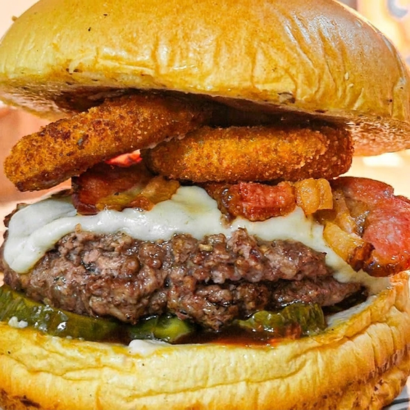 Delicioso Hambúrguer bovino 170gr. Grelhado na brasa, queijo mussarela, Bacon,Onion Rings crocantes e Pickles