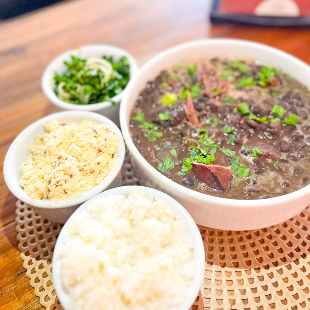 Uma porção deliciosa de feijoada, acompanhada de arroz soltinho, farofa crocante e salada de couve fresquinha.