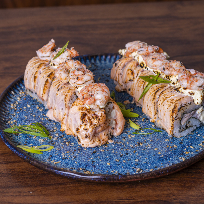 Arroz enrolado no nori com recheio de de salmão e cream cheese. Por cima, tirinhas de salmão com camarões empanados.