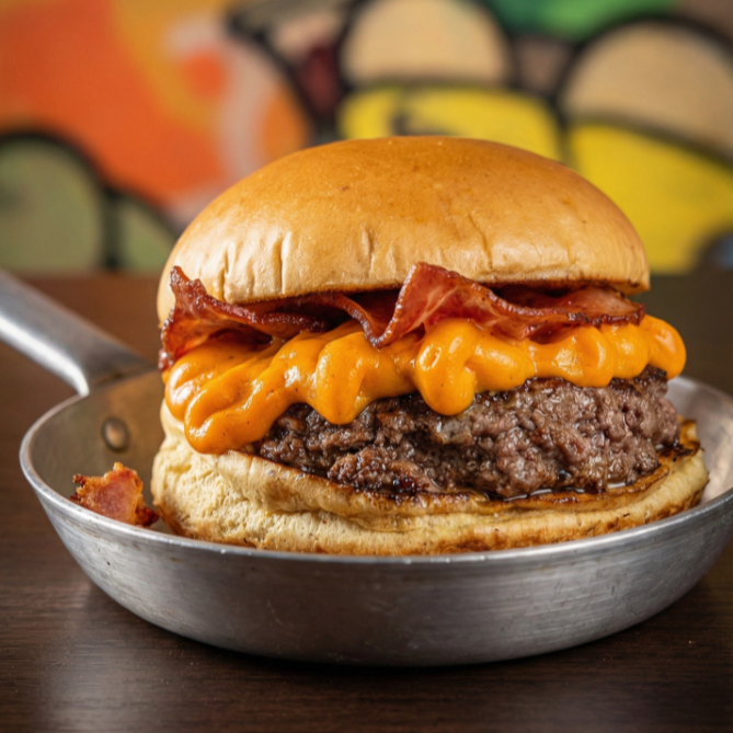 Pão brioche tostado na chapa com manteiga, hamburguer artesanal de aprox 160g, cheddar cremoso, bacon e maionese da casa.