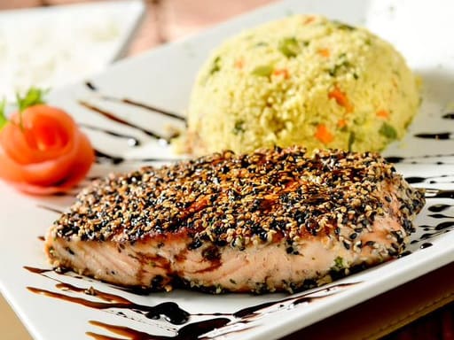 Filé de salmão grelhado com crosta de ger-gelim, molho teriyaki. Acompanha arroz branco e cuscuz marroquino, com brócolis, cenoura, couve-flor, alho, cebola, pimentão.