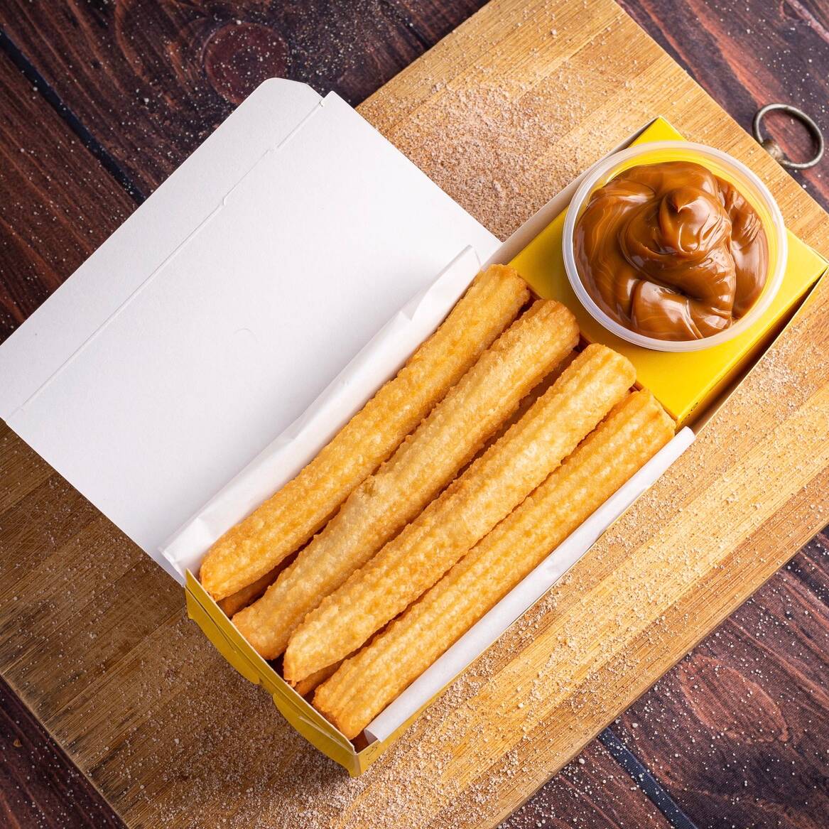 Desfrute de seis irresistíveis churros espanhóis, meticulosamente preparados na hora e envoltos com maestria em uma mistura de açúcar e canela de sabor marcante. Estes churros são sempre entregues perfeitamente sequinhos, garantindo uma textura excepcionalmente crocante e um interior suave, proporcionando uma experiência gastronômica verdadeiramente memorável. Aprecie o autêntico sabor da Espanha em cada mordida desse esplêndido deleite!