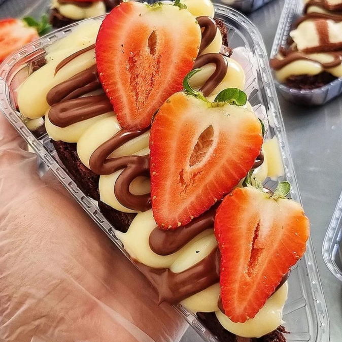 Uma deliciosa fatia de brownie feito com chocolate blend e recheado com brigadeiro cremoso de Ninho com morango e Nutella. Aprox. 130g