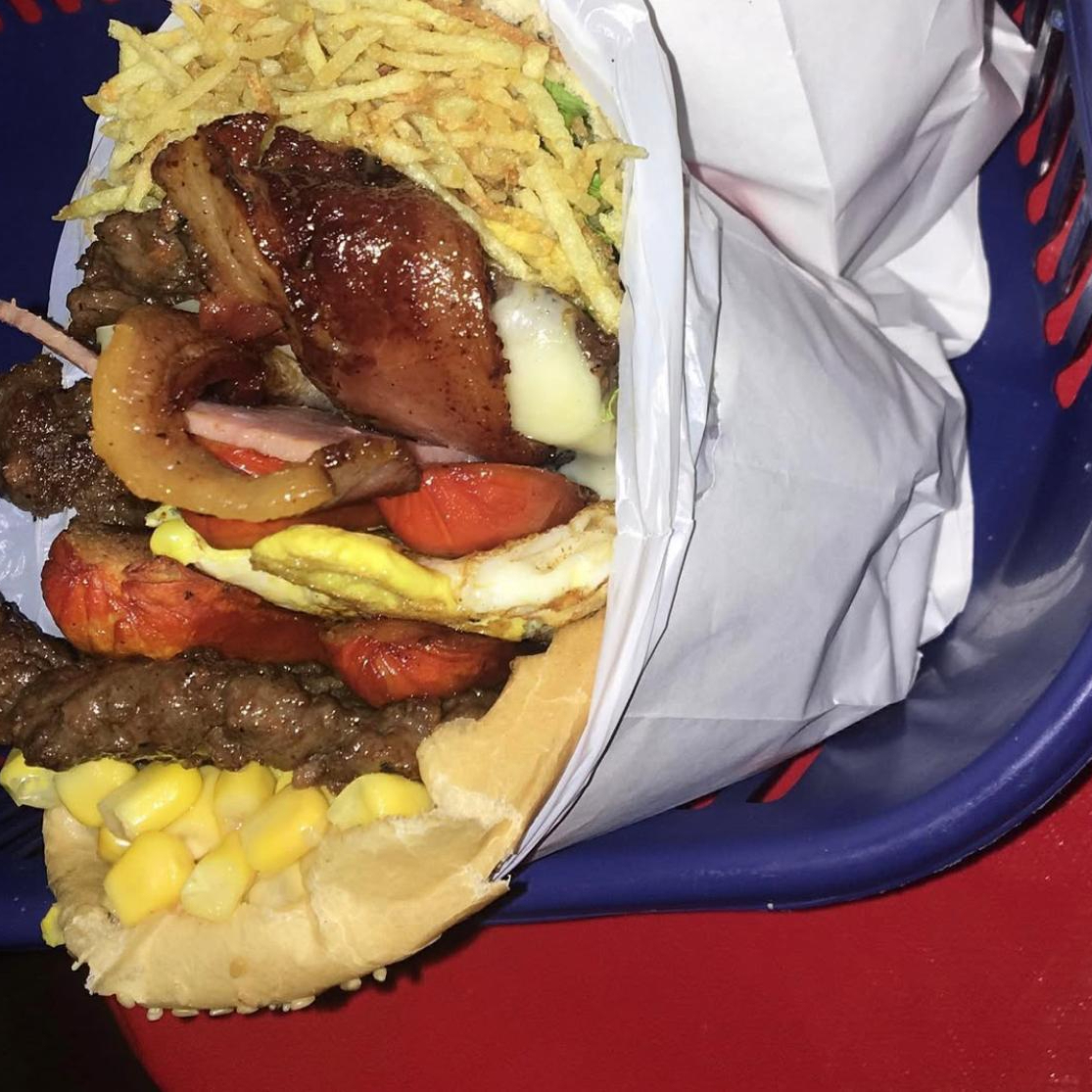 Pão, hamburguer, muçarela, bacon, salsicha, ovo, apresentado, tomate, alface e milho.