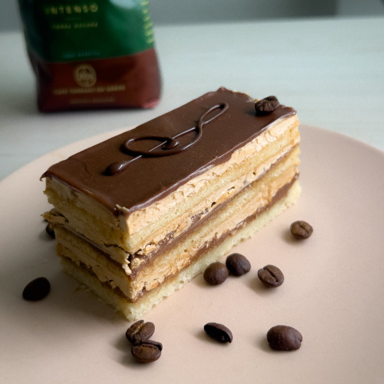Café especial e Chocolate nobre. Apresentamos um dos melhores doces da confeitaria francesa: Ópera. Feito em 9 camadas: ganache de chocolate nobre com caramelo, biscuit joconde de farinha de amêndoas banhado em Café especial arábico, creme de manteiga com merengue italiano e café expresso. Finalizado com uma nota musical no topo e um grão genuíno do café premiado Orfeu, que exala o cheiro maravilhoso de cafeteria nobre. Leve, macio, perfeito para acompanhar um café e um momento relaxante. 150g Não contêm glúten